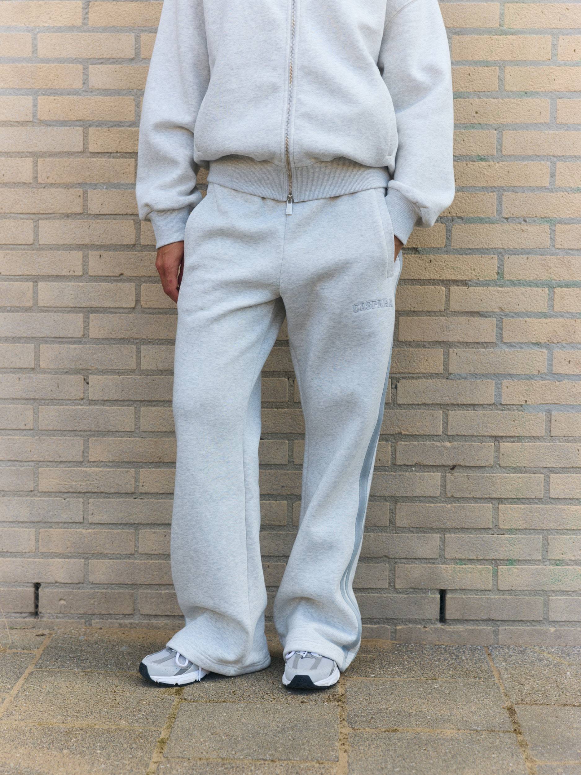 Woman wearing grey melange straight-leg sweatpants with side piping against a brick wall.